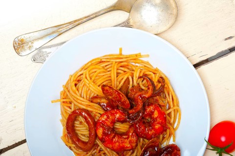 Italian seafood spaghetti pasta on red tomato sauce over white rustic wood table