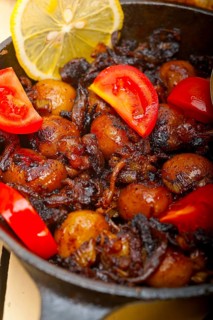 Baby cuttle fish roasted on iron skillet with tomatoes and onions over rustic wood table