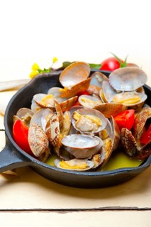 Fresh clams stewed on an iron skillet over wite rustic wood table