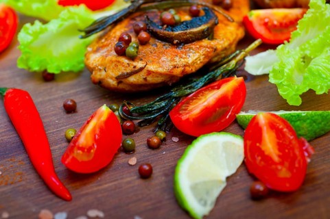 Wood fired hoven cooked chicken breast on wood board with herbs spices and vegetables