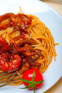 Italian seafood spaghetti pasta on red tomato sauce over white rustic wood table