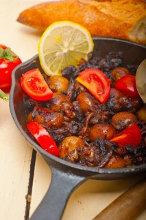 Baby cuttle fish roasted on iron skillet with tomatoes and onions over rustic wood table