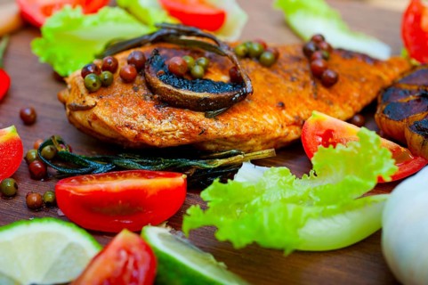 Wood fired hoven cooked chicken breast on wood board with herbs spices and vegetables