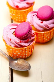Fresh pink berry cream cupcake with macaroon on top over rustic wood table