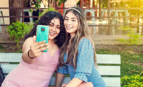 Two pretty girls sitting on a bench taking a selfie