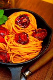Italian spaghetti pasta and tomato with mint leaves on iron skillet over wood board