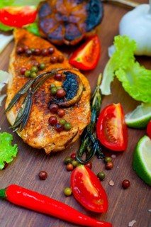Wood fired hoven cooked chicken breast on wood board with herbs spices and vegetables