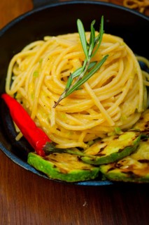 Italian spaghetti pasta with zucchini sauce on iron skillet over wood board