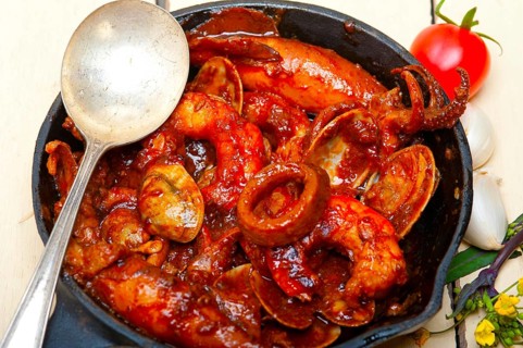 Fresh seafood stew prepared on an iron skillet ove white rustic wood table