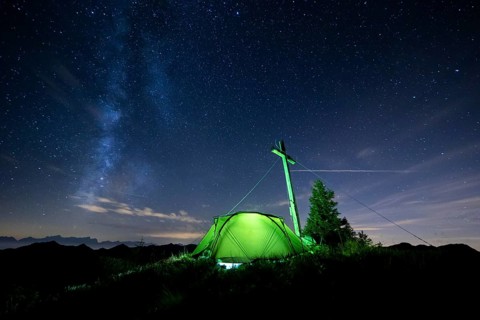 Green tent with summit cross under a starry sky on Portlakopf