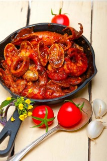 Fresh seafood stew prepared on an iron skillet ove white rustic wood table