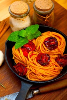 Italian spaghetti pasta and tomato with mint leaves on iron skillet over wood board