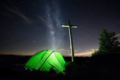 Green tent with summit cross under a starry sky on Portlakopf