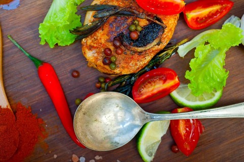 Wood fired hoven cooked chicken breast on wood board with herbs spices and vegetables