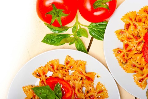 Italian pasta farfalle butterfly bow-tie with tomato basil sauce over white rustic wood table