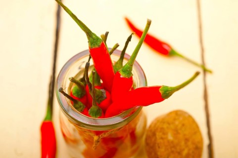 Red chili peppers on a glass jar over white wood rustic table