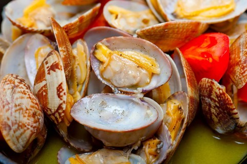 Fresh clams stewed on an iron skillet over wite rustic wood table