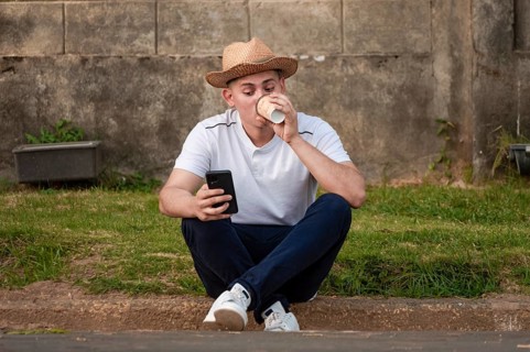 Young man sitting on sidewalk checking phone