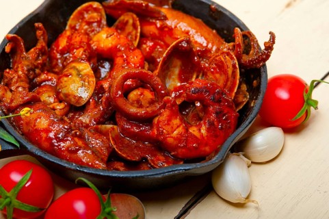 Fresh seafood stew prepared on an iron skillet ove white rustic wood table