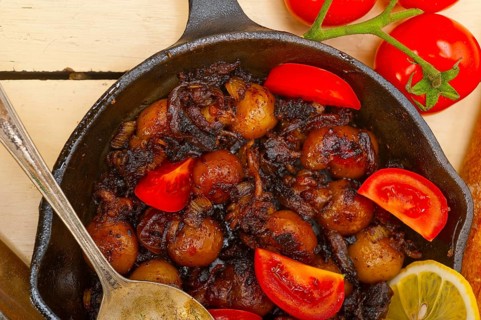 Baby cuttle fish roasted on iron skillet with tomatoes and onions over rustic wood table