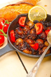 Baby cuttle fish roasted on iron skillet with tomatoes and onions over rustic wood table