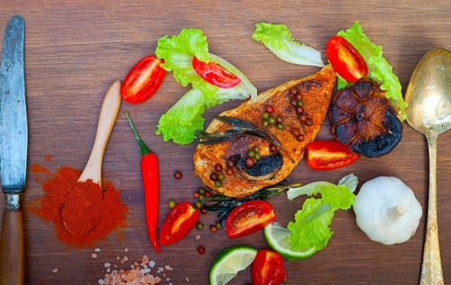 Wood fired hoven cooked chicken breast on wood board with herbs spices and vegetables
