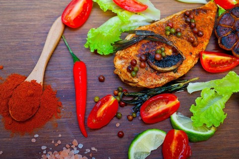 Wood fired hoven cooked chicken breast on wood board with herbs spices and vegetables