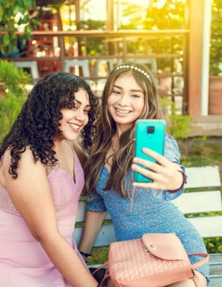 Two pretty girls sitting on a bench taking a selfie