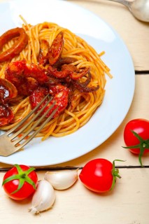 Italian seafood spaghetti pasta on red tomato sauce over white rustic wood table
