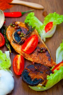Wood fired hoven cooked chicken breast on wood board with herbs spices and vegetables