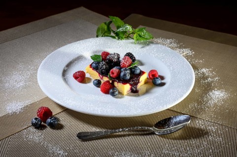 A slice of cheesecake with fresh raspberries and blackberries and a layer of icing sugar on a white plate