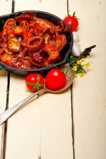 Fresh seafood stew prepared on an iron skillet ove white rustic wood table