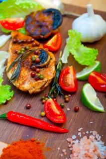Wood fired hoven cooked chicken breast on wood board with herbs spices and vegetables