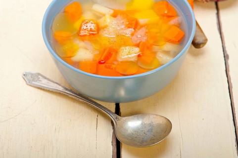 Traditional Italian minestrone soup on a rustic table with ingredients