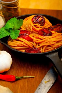 Italian spaghetti pasta and tomato with mint leaves on iron skillet over wood board