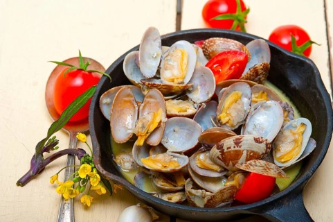 Fresh clams stewed on an iron skillet over wite rustic wood table