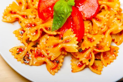Italian pasta farfalle butterfly bow-tie with tomato basil sauce over white rustic wood table