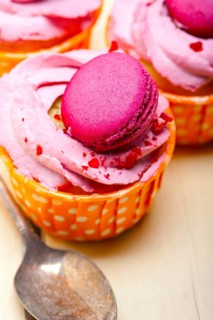 Fresh pink berry cream cupcake with macaroon on top over rustic wood table