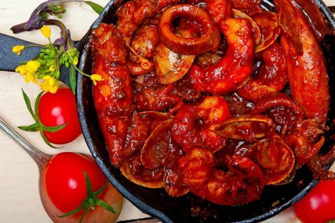 Fresh seafood stew prepared on an iron skillet ove white rustic wood table