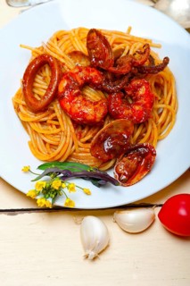 Italian seafood spaghetti pasta on red tomato sauce over white rustic wood table