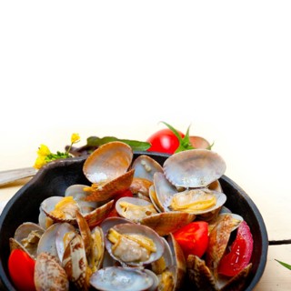 Fresh clams stewed on an iron skillet over wite rustic wood table
