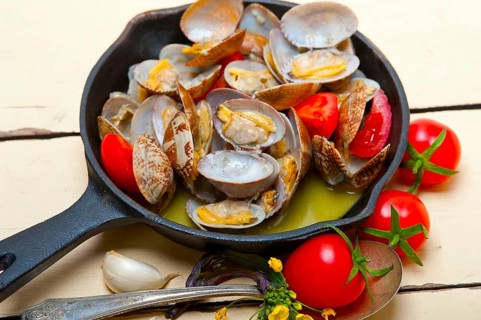 Fresh clams stewed on an iron skillet over wite rustic wood table