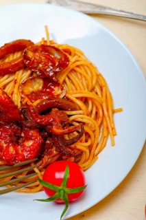 Italian seafood spaghetti pasta on red tomato sauce over white rustic wood table