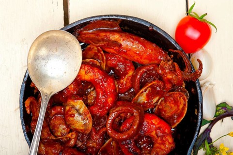 Fresh seafood stew prepared on an iron skillet ove white rustic wood table