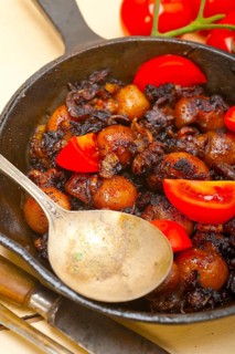 Baby cuttle fish roasted on iron skillet with tomatoes and onions over rustic wood table