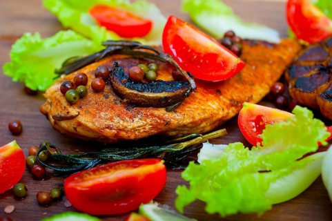 Wood fired hoven cooked chicken breast on wood board with herbs spices and vegetables