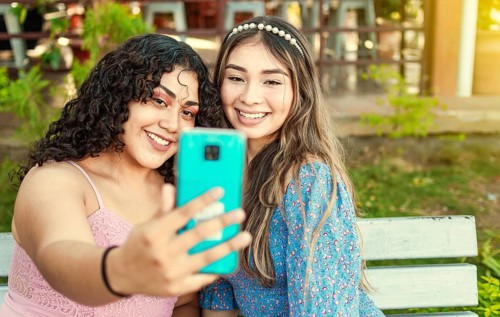 Two pretty girls sitting on a bench taking a selfie