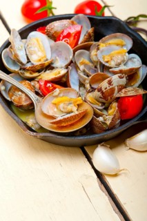 Fresh clams stewed on an iron skillet over wite rustic wood table