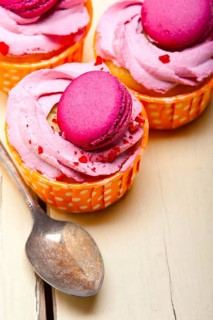 Fresh pink berry cream cupcake with macaroon on top over rustic wood table