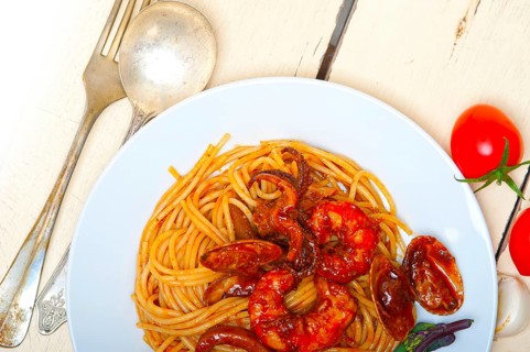 Italian seafood spaghetti pasta on red tomato sauce over white rustic wood table